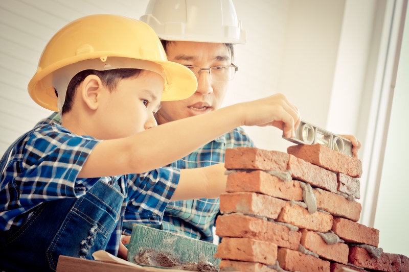 Un enfant qui monte un mur de briques avec l’aide d’un adulte. 