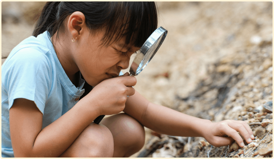 Une jeune fille regarde des roches avec une loupe. 