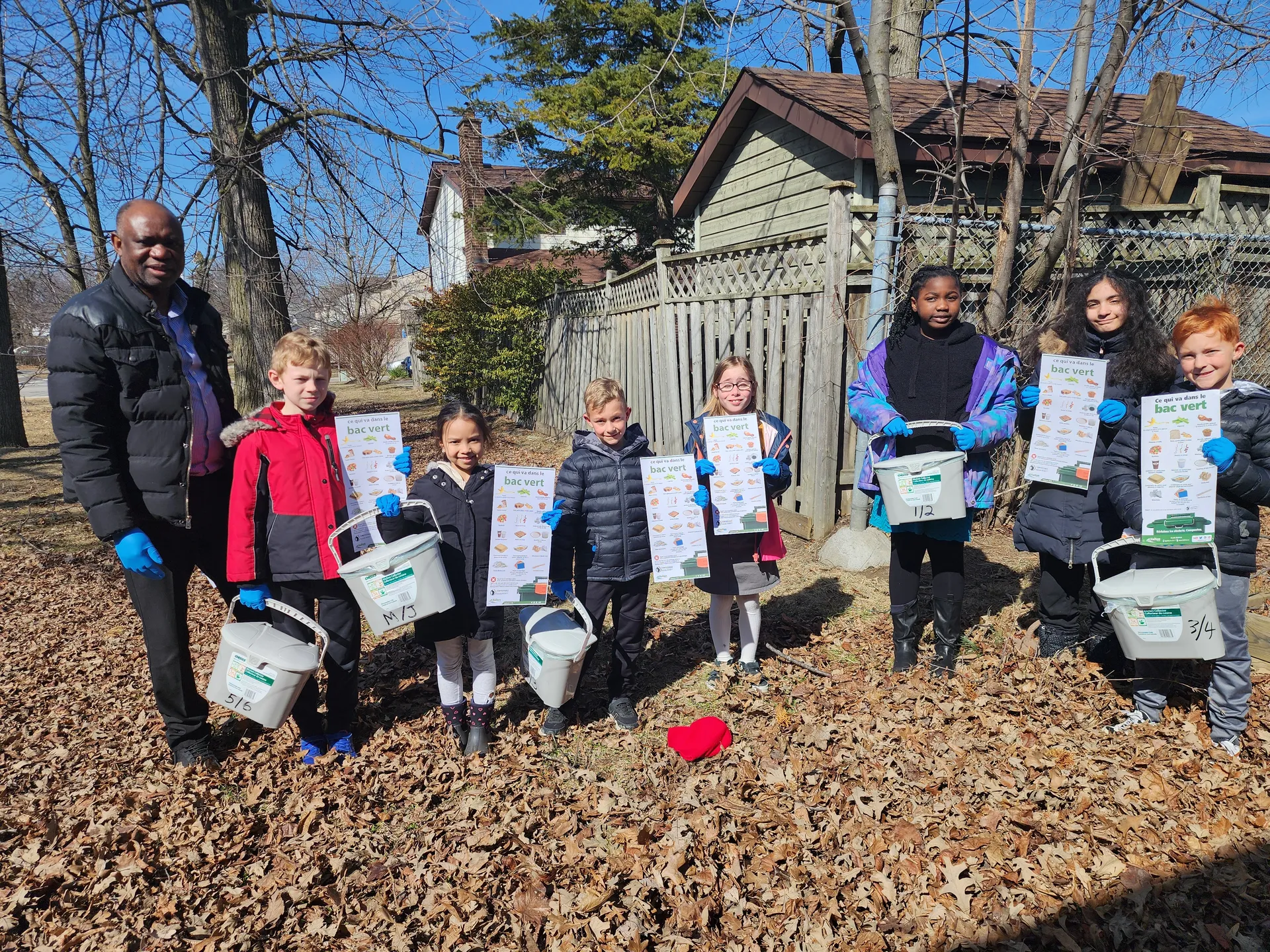 Photo d'un adulte et de sept enfants tenant chacun une affiche et un petit conteneur à compost.