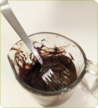 Photo sur laquelle on peut voir une tasse à mesurer remplie de chocolat fondu. On utilise une fourchette pour mélanger le chocolat. 