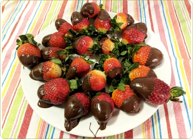 Photo d’une assiette remplie de fraises trempées dans le chocolat. 