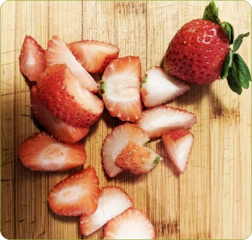 Photo sur laquelle on peut voir des morceaux de fraises tranchées sur une planche à découper.  