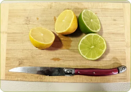 Photo sur laquelle on peut voir un citron, une lime et un couteau sur une planche à découper. 