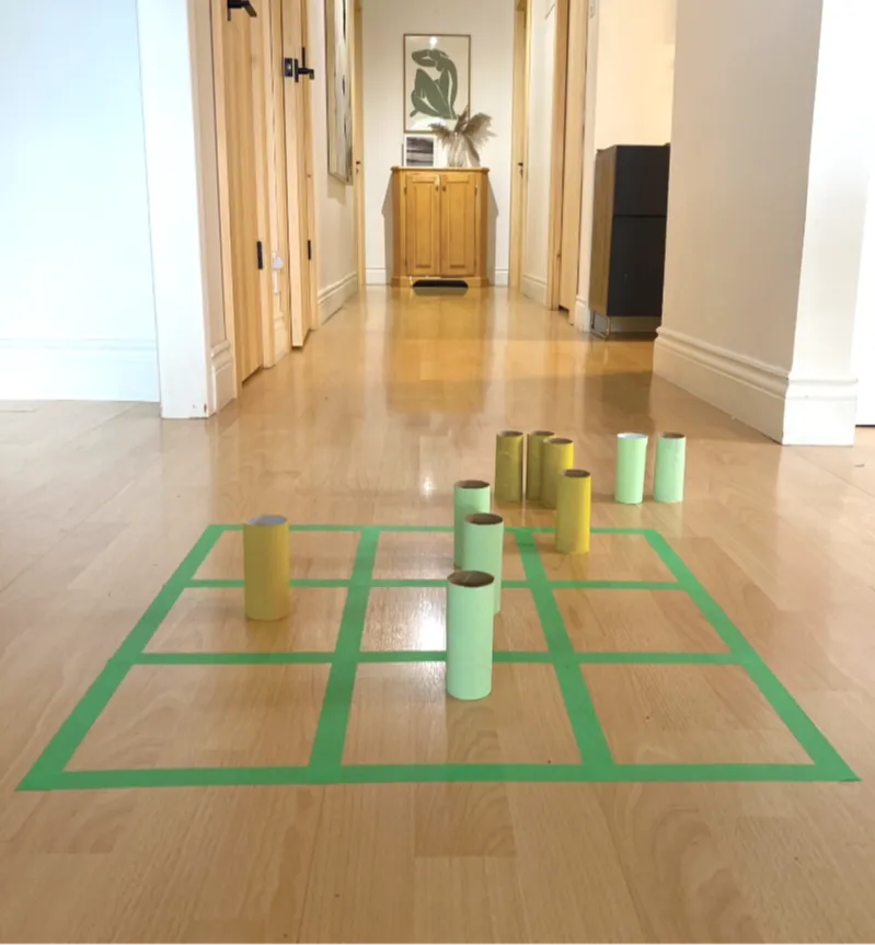 Image d’un jeu de tic-tac-toe à relais. La grille est réalisée à l’aide de papier adhésif et des rouleaux de papier hygiénique vides peinturés en vert et en jaune remplacent les X et les O. 